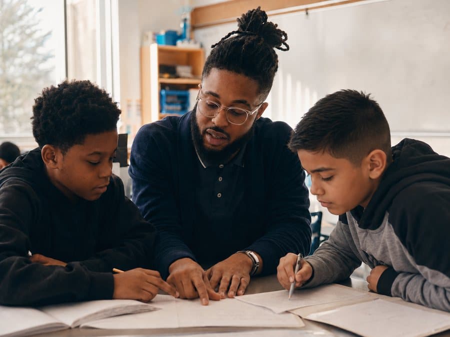 A teacher working through a workbook with two boys at a classroom table